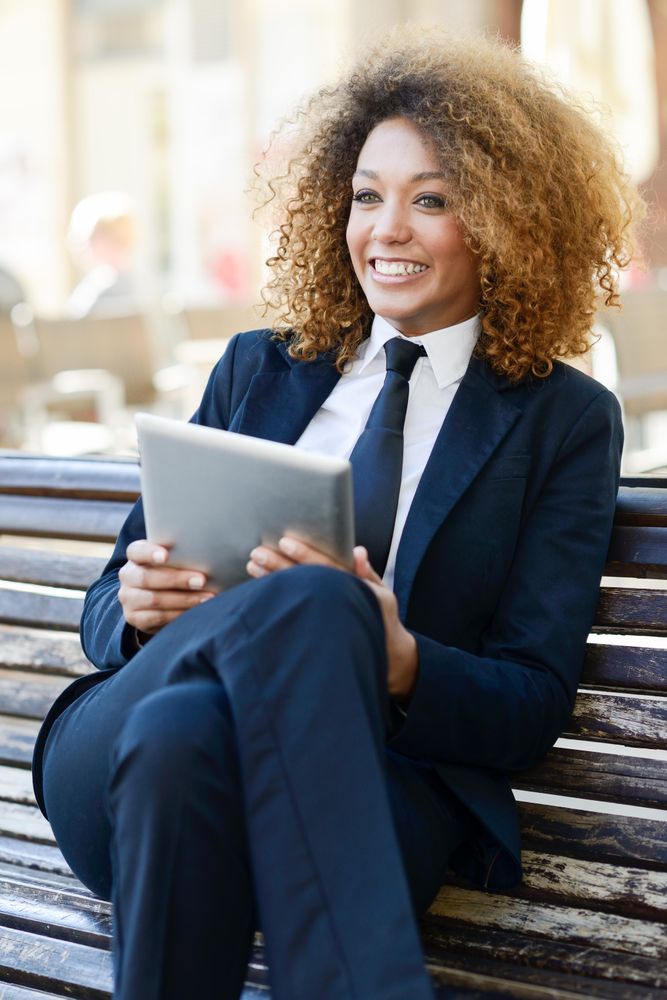 Happy woman in suit using her digital tablet on outdoor bench