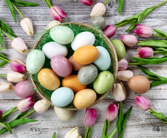 Happy Easter concept with basket filled of colorful eggs on weathered wood. Overhead view layout