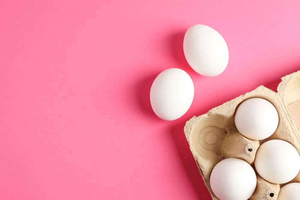 Chicken eggs in carton box on pink background, space for text