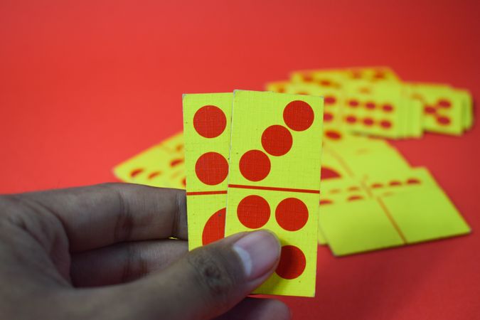 Hand holding domino cards over red table