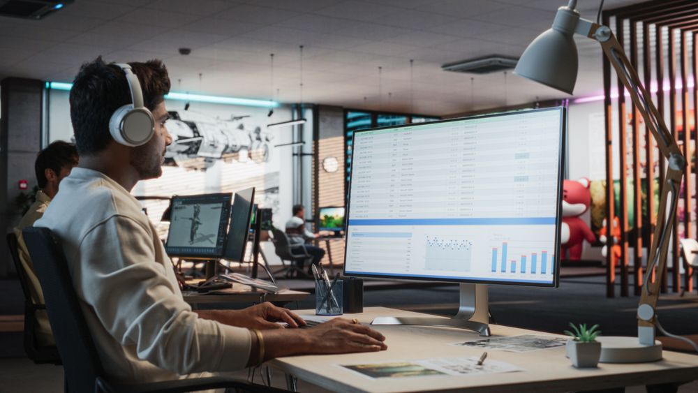 Indian Male Manager Using Desktop Computer With Analytics Software wth Financial Reports.