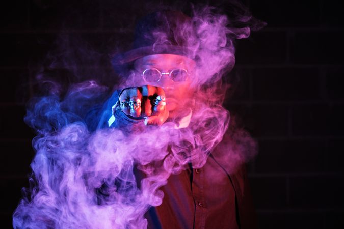 Stylish Black man surrounded by vapor in darkness