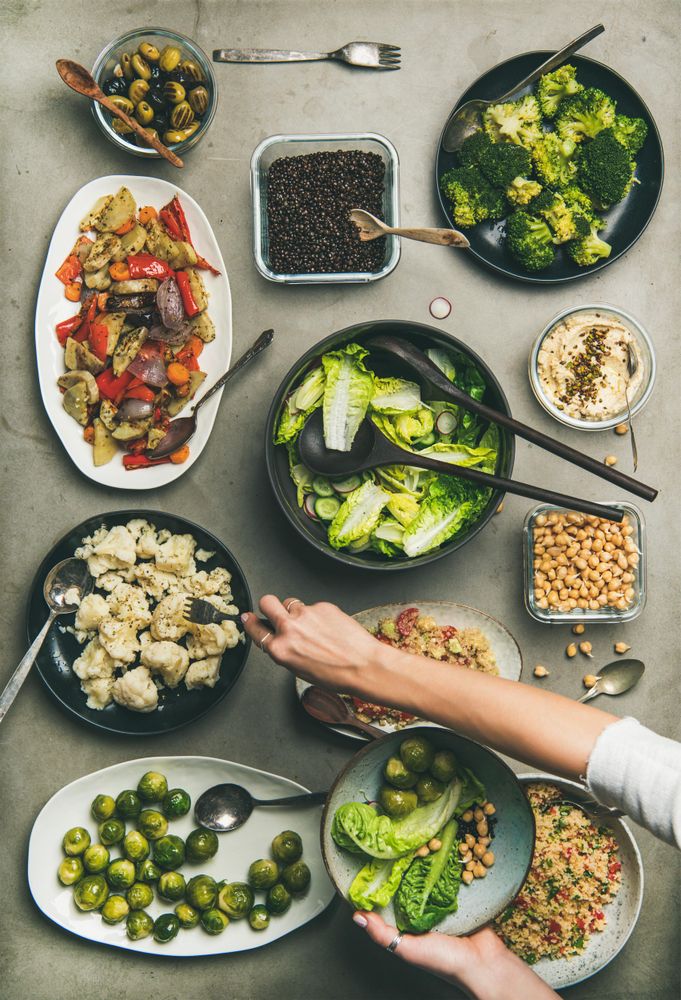 Vegan dinner table setting with healthy dishes in plates on table and woman’s hands taking food