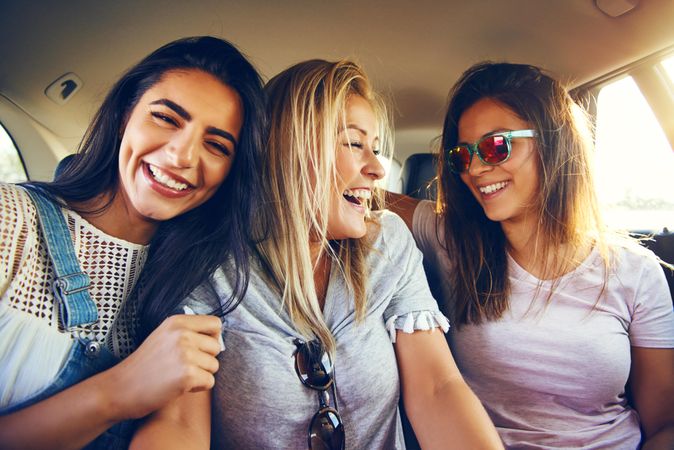 Group of smiling female friends laughing with each other while riding in back of vehicle