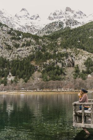 Woman on seat near wonderful lake between hills in snow and cloudy sky