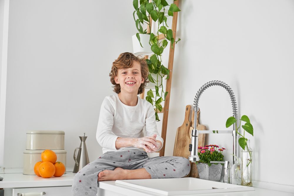 Smiling boy washing hands with soap in morning