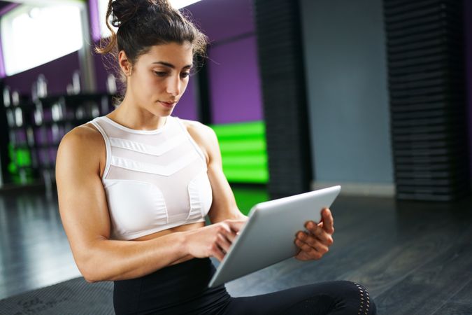 Fit woman cross legged on yoga mat reading a digital tablet