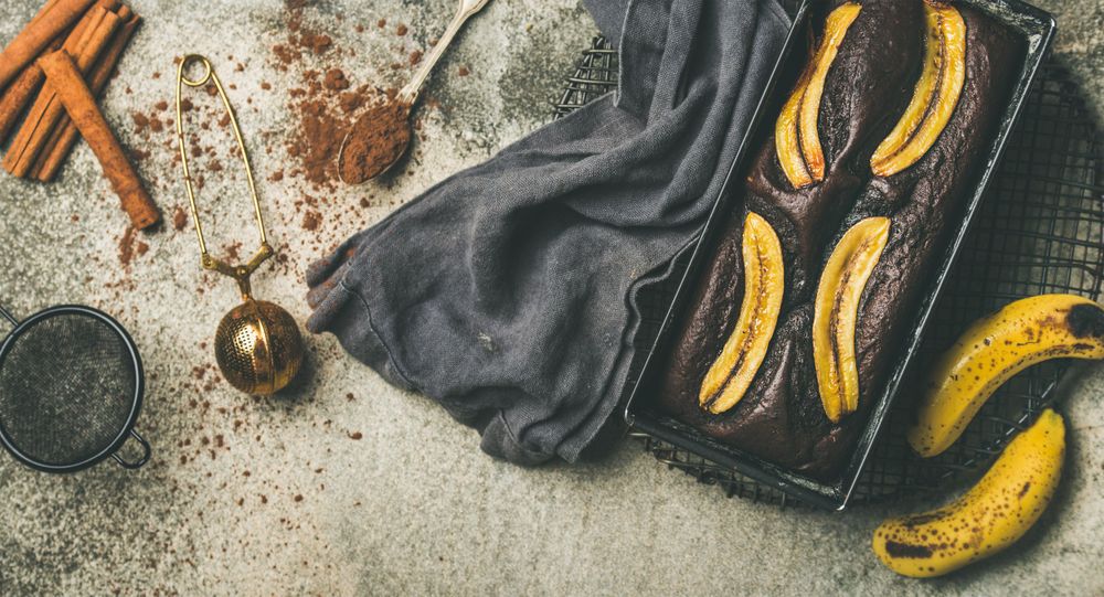 Freshly baked dark chocolate banana bread cake on concrete counter, with cinnamon and cocoa powder