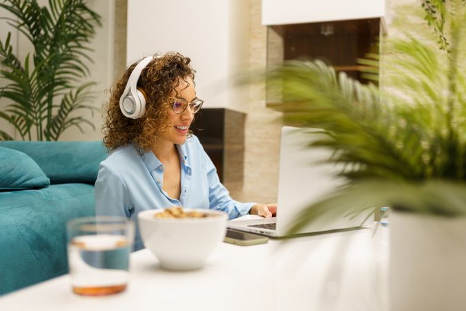 Young woman in headphones using laptop while sitting by coffee table in room