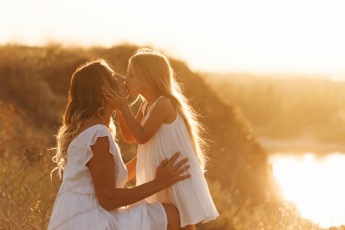 A little girl and mother kiss by lake at dusk