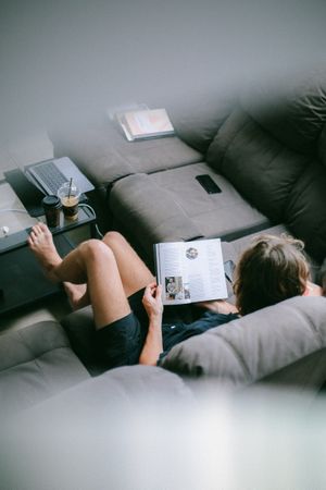 Top view of woman reading a book sitting on couch in living room