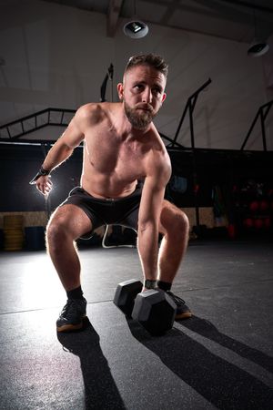 Concentrated athlete practicing fitness with dumbbell in sport