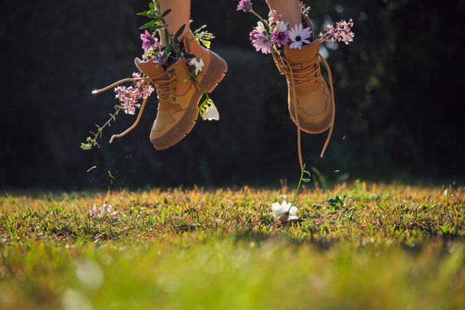 Crop person in boots with flowers jumping on grassy meadow