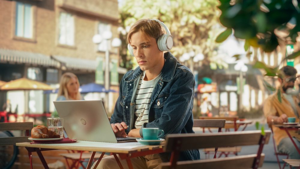 Handsome Man Using Laptop Computer on a Terrace in a Cozy Cafe on a Summer Day.