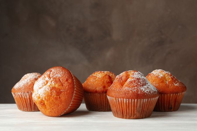 Tasty muffins on wooden table against brown background