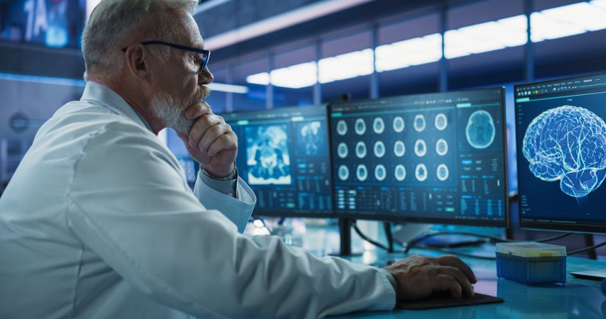 Male Neuroscientist Using Desktop Computer To Analyze MRI Scans Of Brain In Medical Research Center Laboratory.