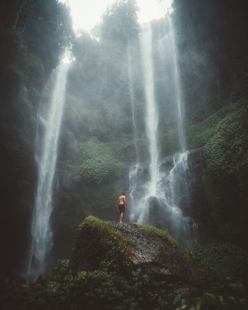 Tourist on rock under hazy waterfall
