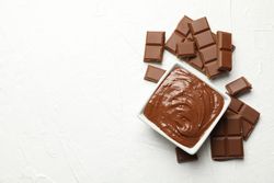 Bowl with chocolate and chocolate pieces on neutral background