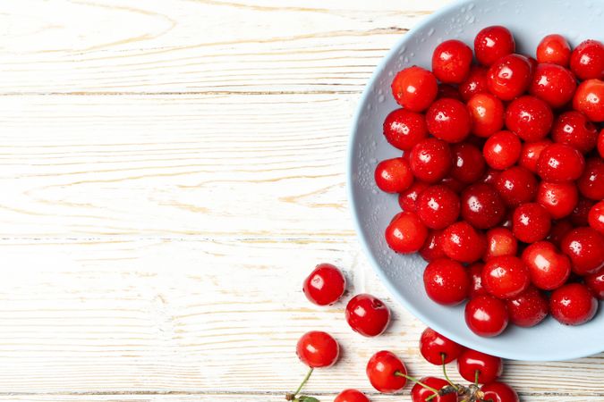 Plate with red cherry on wooden background, top view