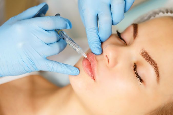Hands in latex gloves injecting beauty treatment into upper lip