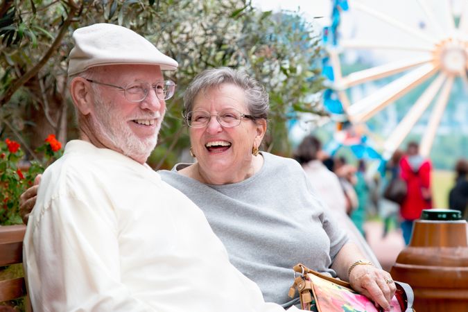 Laughing Adult Couple Enjoying The Carnival From the Outdoor Bench.