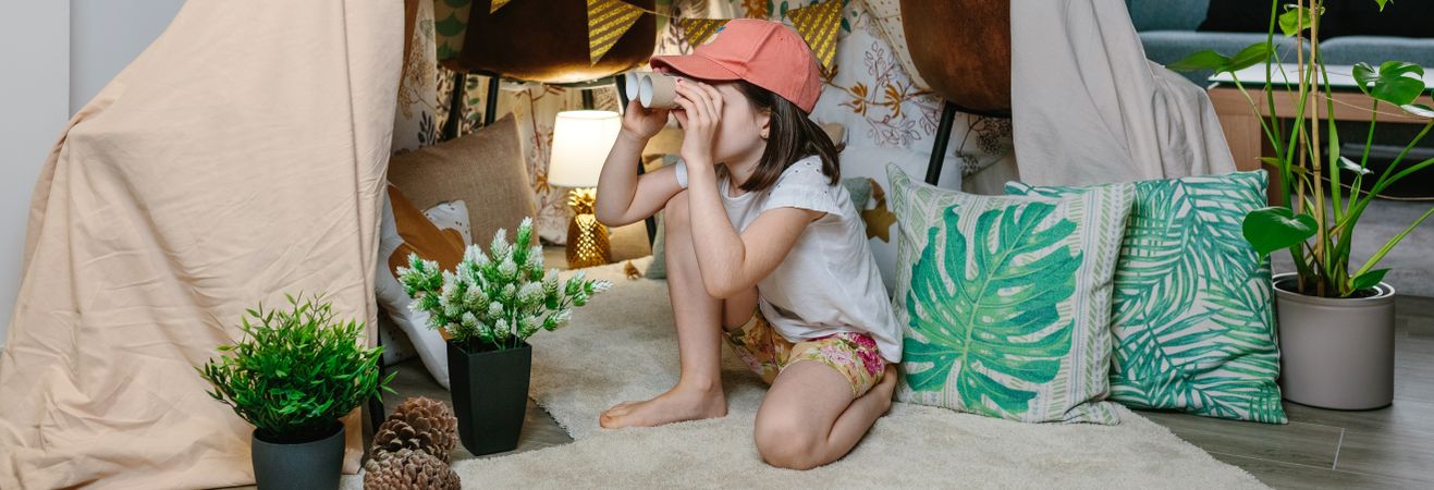Girl playing with cardboard binoculars while camping at home