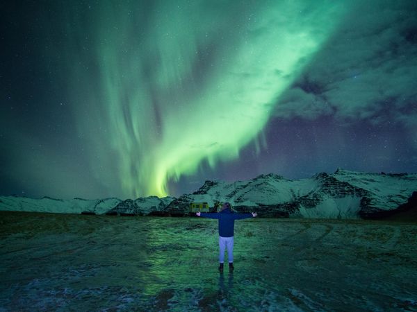 Person opening their arms standing under aurora borealis