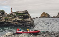 Woman on rough cliff near paddle board
