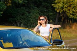 Woman talking on cell phone standing outside of her yellow car 5RxNBb