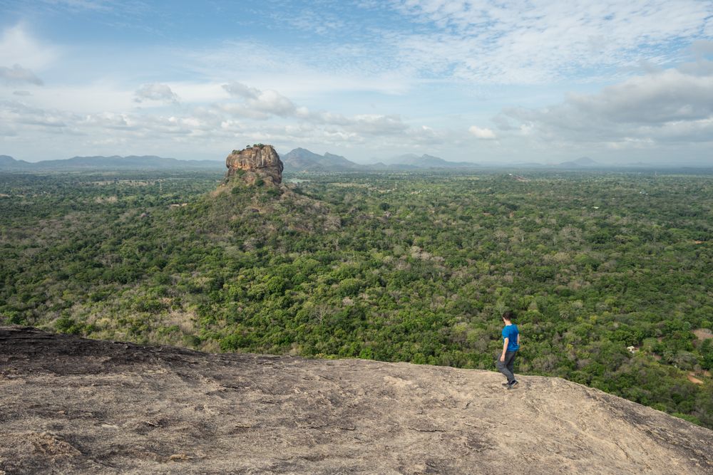 Tourist against solitary rock in middle of green forested plain under clear sky in summer