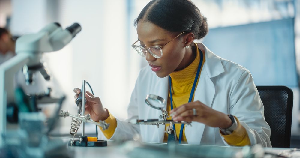 Portrait of Black Female Lab Specialist Carefully Soldering a Circuit Board in a Manufacturing Industrial Company.