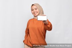 Confident Muslim woman smiling while holding up smart phone with mock up screen 0P8l70