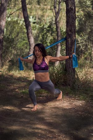 Athletic woman training with elastic band in forest