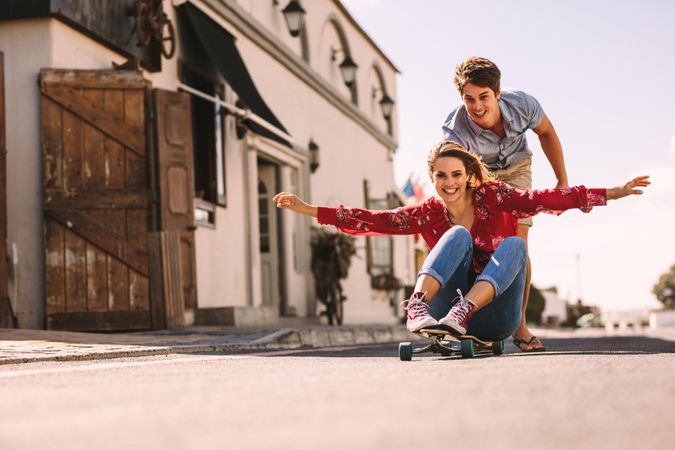 Smiling woman sitting on a skateboard riding down an empty street