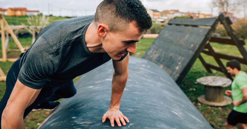 Man in an obstacle course climbing a drum