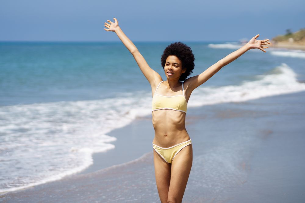 Female wearing yellow bikini with open arms at the beach