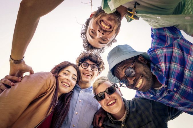 Low angle view of happy diverse friends in a huddle looking down at camera.
