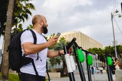 Traveler with backpack browsing smartphone and choosing electronic scooter