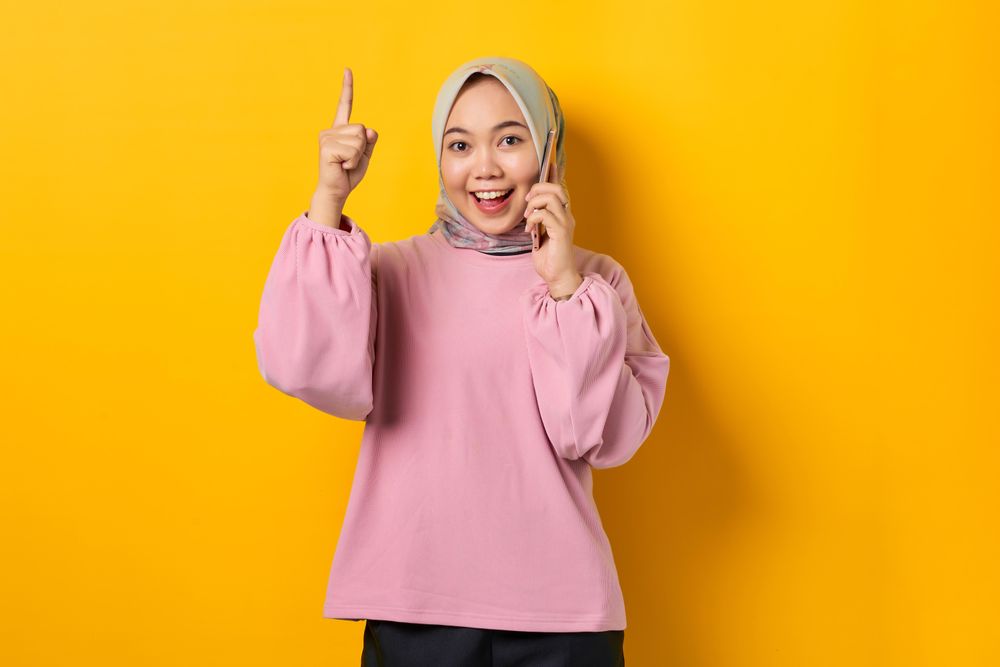Excited Muslim woman on the phone and pointing upwards with good idea