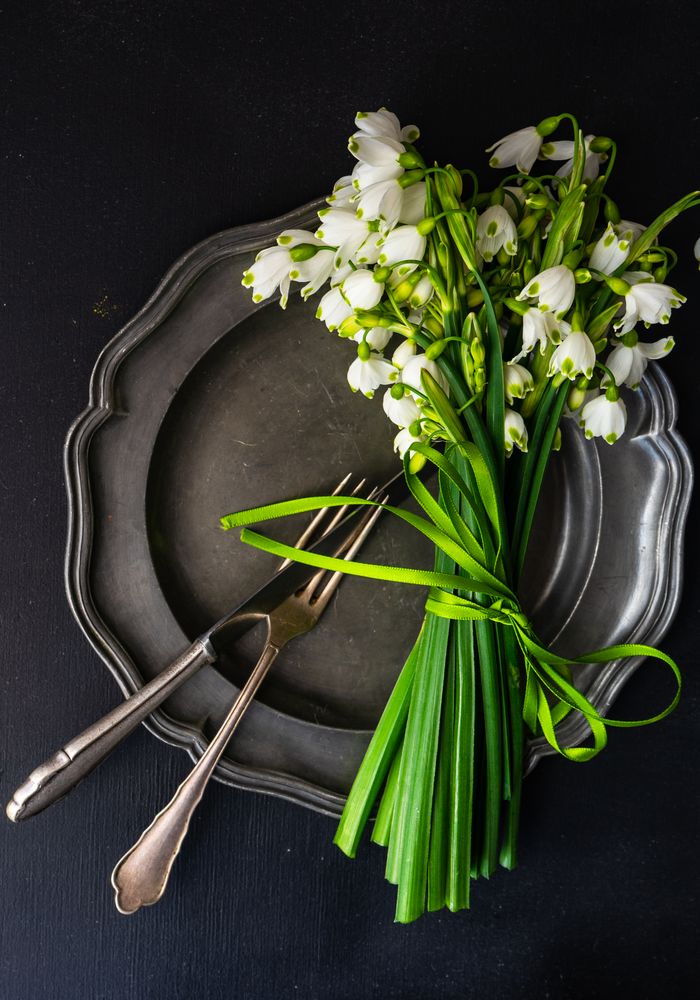 Table setting for Easter dinner with snowdrop flowers on dark plate