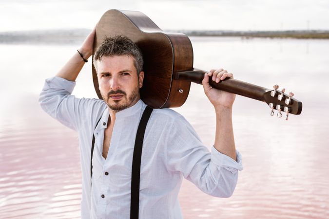 Musician gazing and carrying guitar behind back while standing on beach