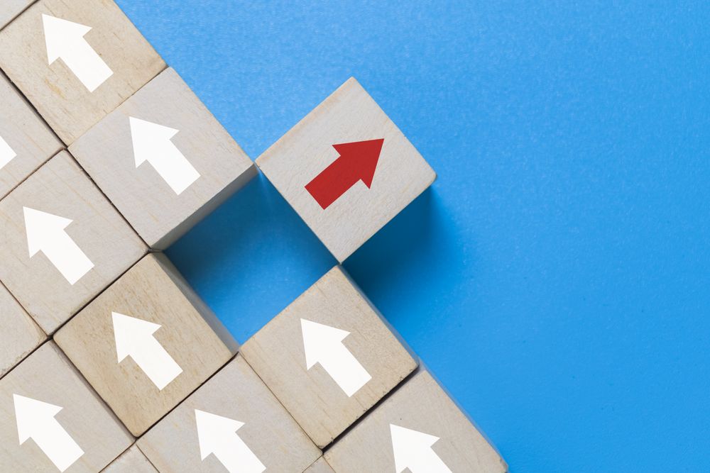 wooden blocks with arrows and one different direction red arrow isolated on blue background. leadership concept