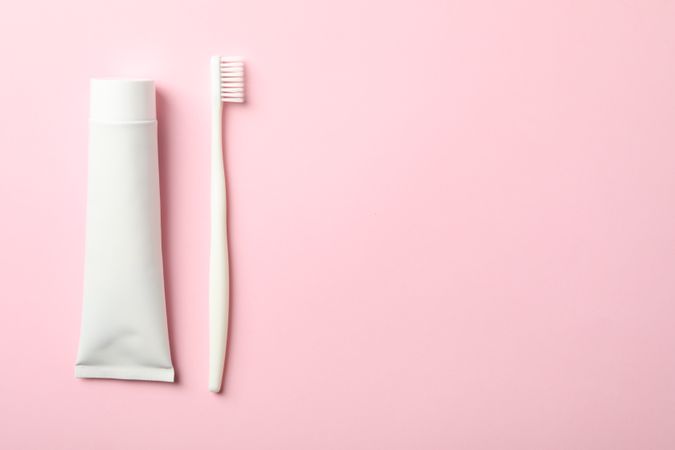 Toothbrush and toothpaste on pink background, space for text