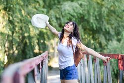 Smiling woman standing on foot bridge in forest with arms opened
