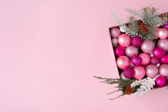 Box of pink festival baubles and branches on pink background
