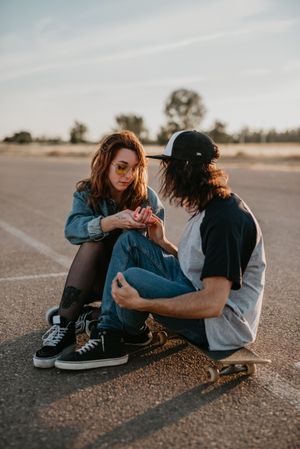 Skaters sitting on empty rural road chatting in sunlight