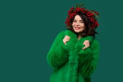 Smiling woman in green coat and red berry wreath posing.