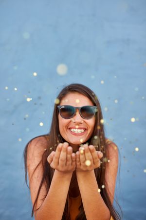 Shot of cheerful young woman blowing sparkles over blue background