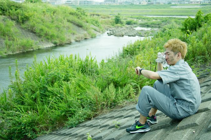 Side view of exhausted man sitting on concrete ground near river stream