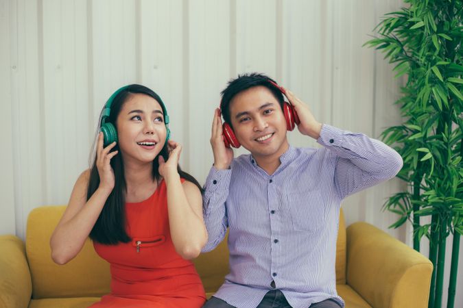 Man and woman having fun listening to headphones on yellow couch